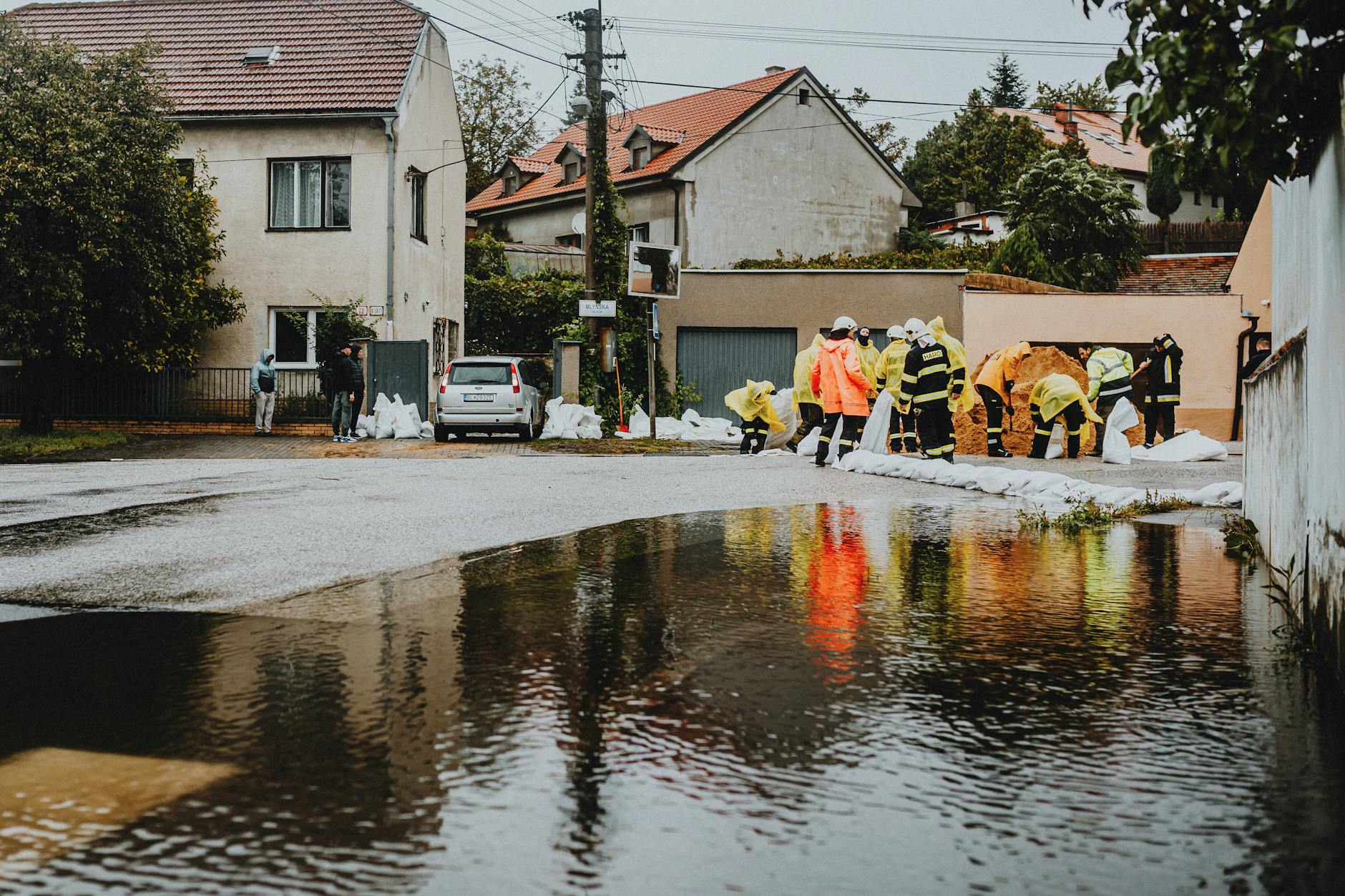 Ratownicy w odblaskowych strojach zabezpieczają zalaną ulicę przy domach